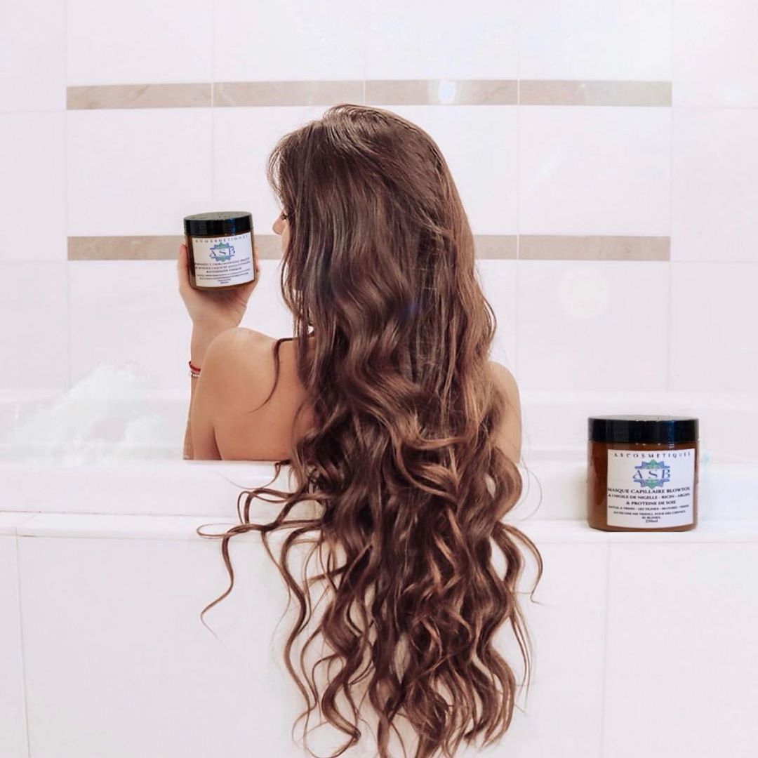 femme de dos dans la baignoire avec les cheveux sortant de la baignoire avec le pot du masque capillaire blowtox dans la main gauche