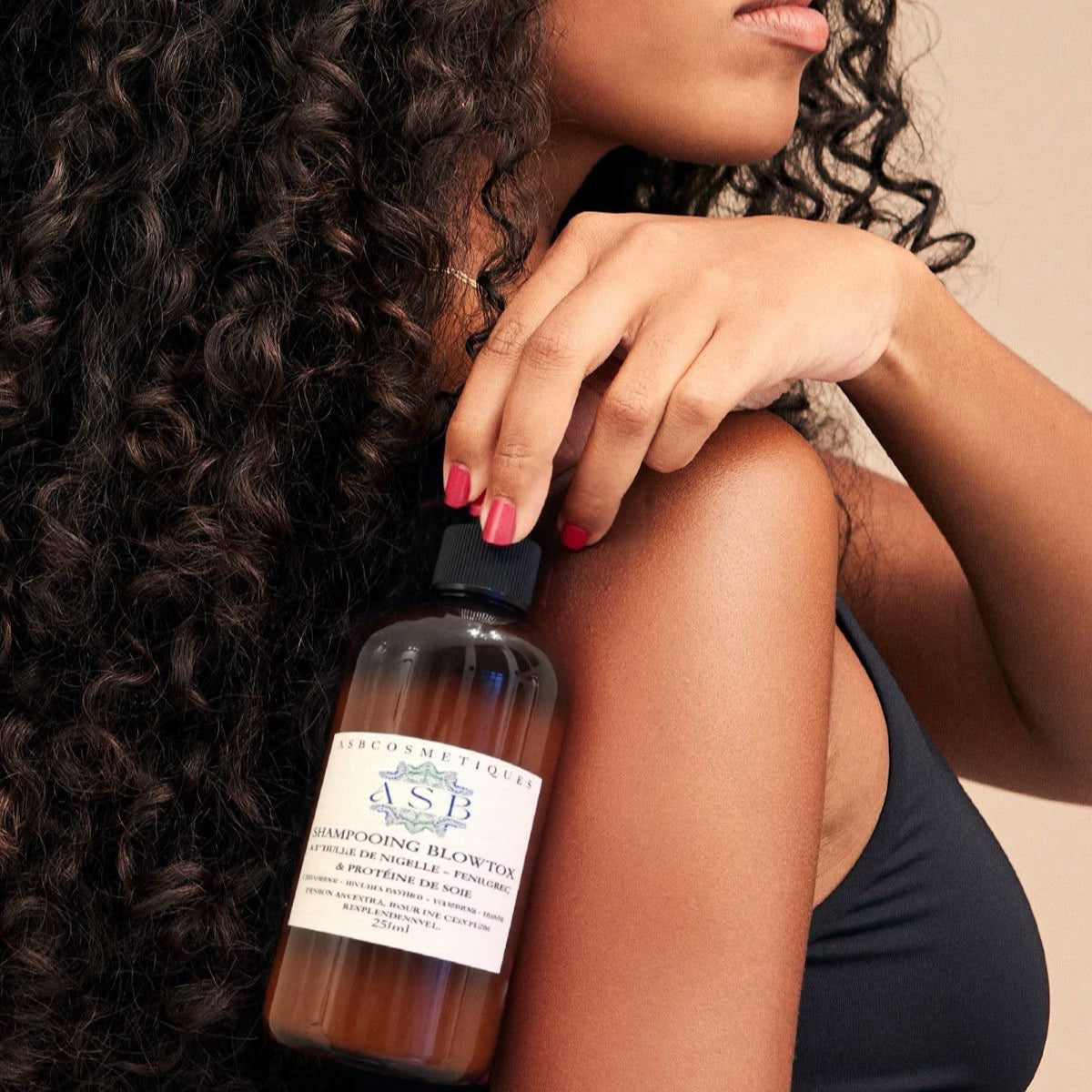 femme tenant la bouteille de shampoing blowtox avec les bout des doigts sur son dos